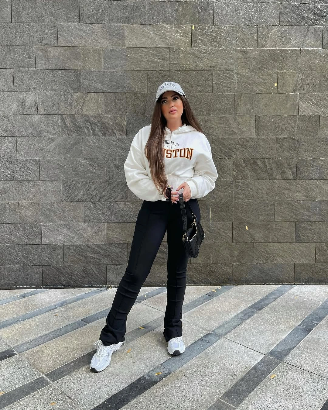 Woman wearing white printed sweatshirt, black pants, light cap, and sneakers