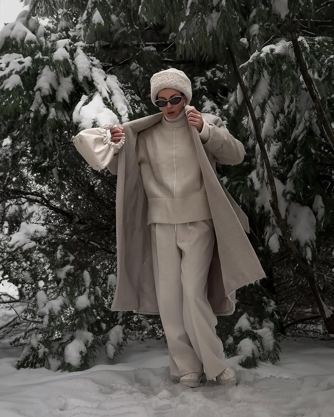 Woman wearing pale coat, cream sweater, wide trousers, and knit hat