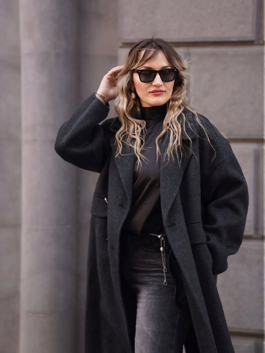 Woman in charcoal coat, black top, dark jeans, and sunglasses