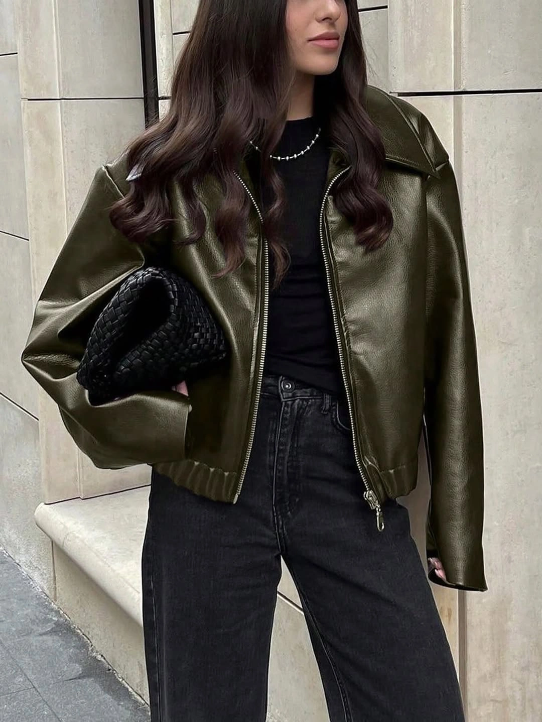 Glossy olive jacket over black top with dark jeans and clutch