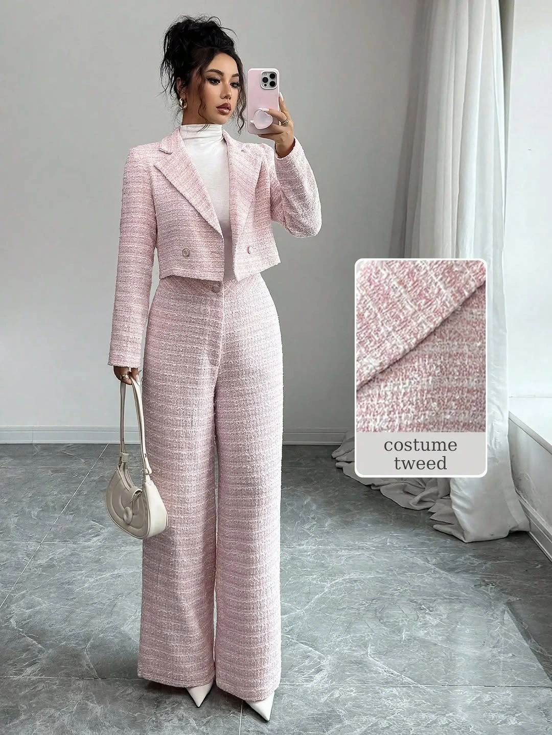 Woman wearing pale pink textured jacket and matching trousers with white handbag