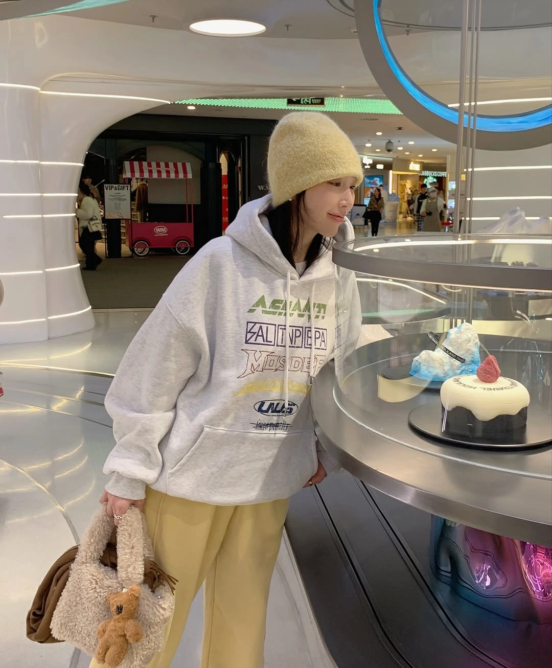 Woman wearing gray printed hoodie, pale yellow trousers, and light knit hat