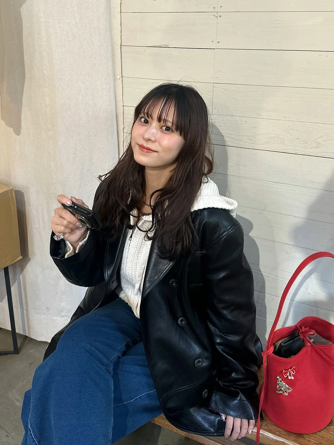 Black leather-look jacket over white hood and blue jeans with red bag