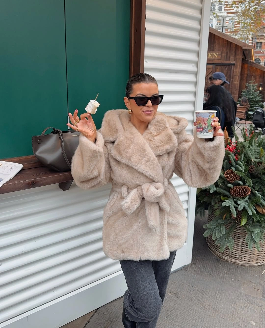 Beige plush wrap jacket with tied waist, gray jeans, and black sunglasses