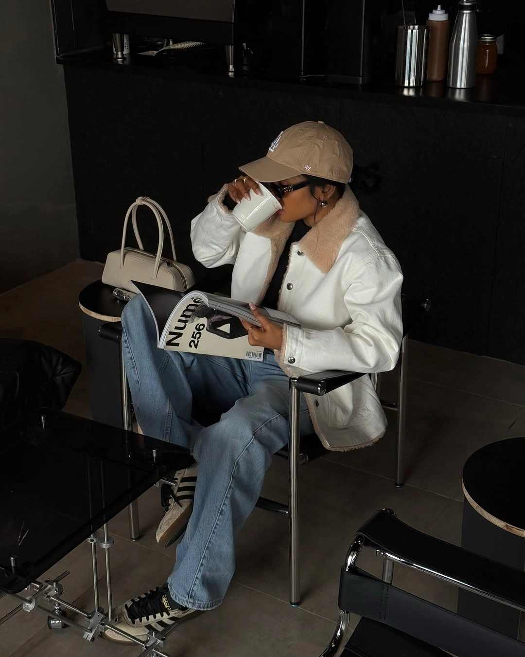 White button-front jacket, beige baseball cap, loose jeans, and cream handbag