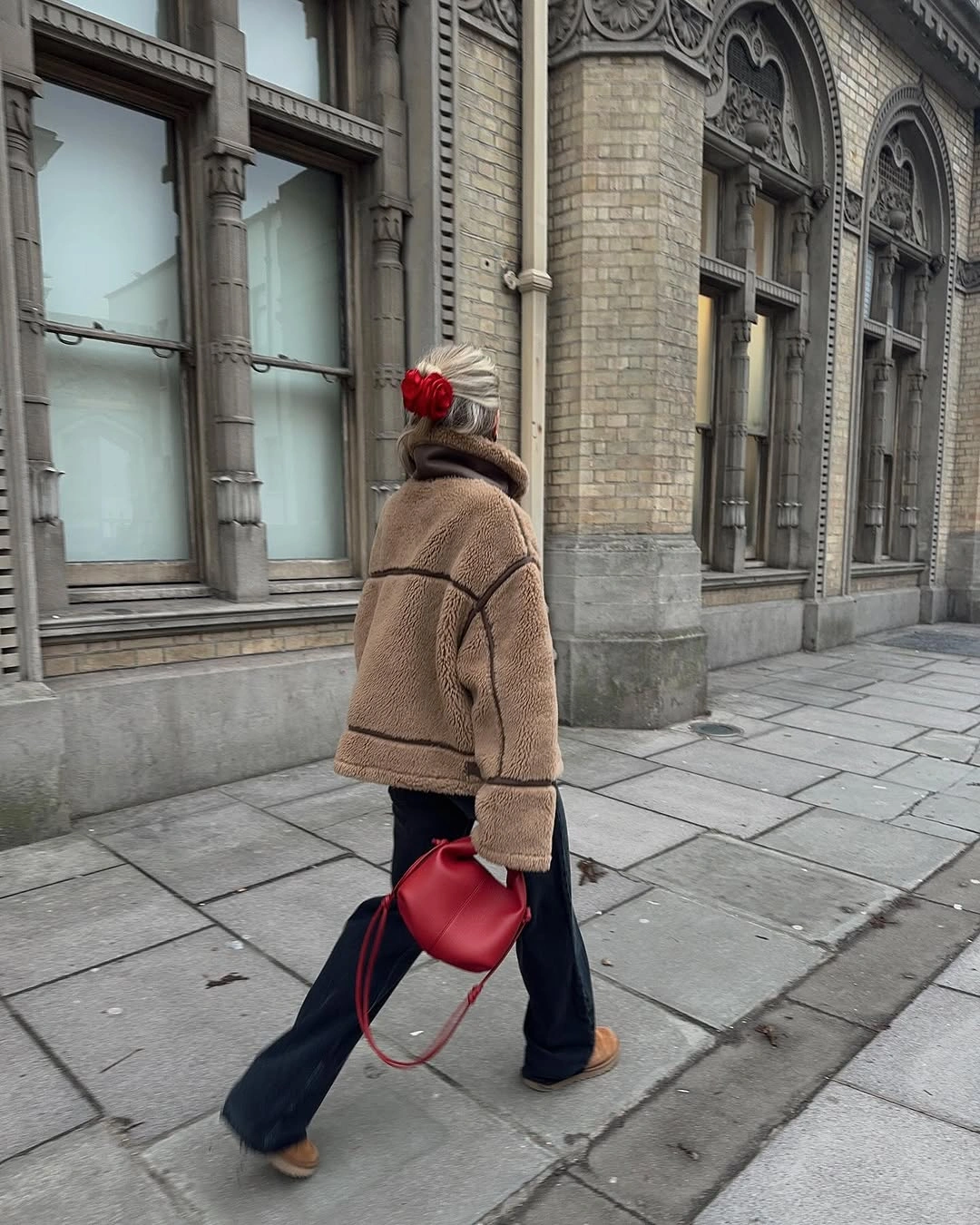 Tan jacket with dark seams, wide jeans, pom-pom hat, and red handbag