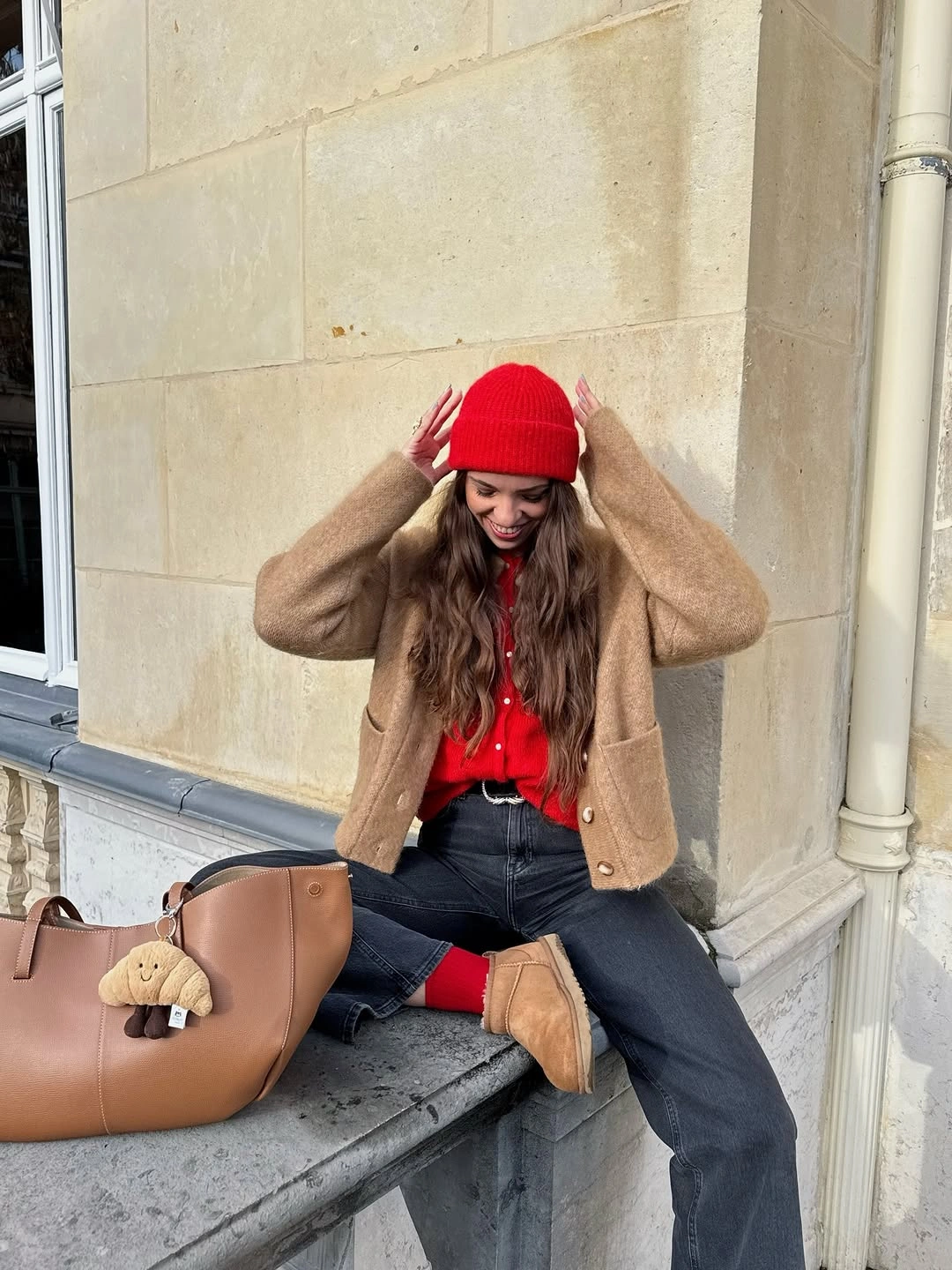 Red beanie and top with tan cardigan, gray jeans, and tan tote