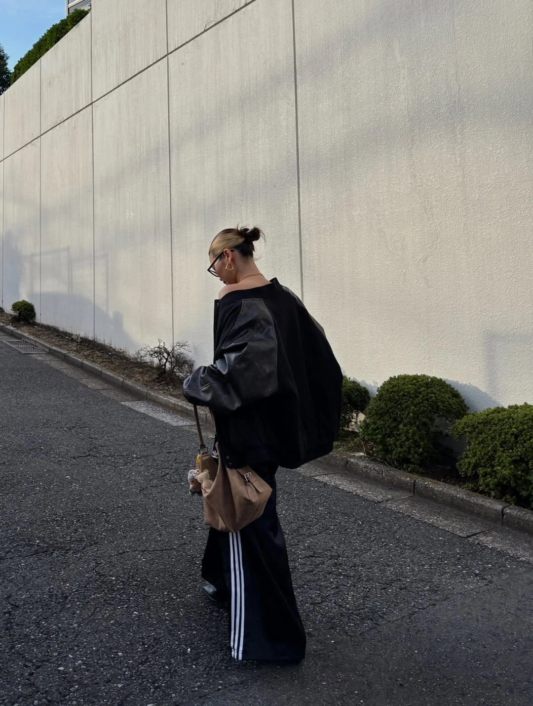Oversized black silhouette with gray sleeve, striped dark trousers, and brown bag