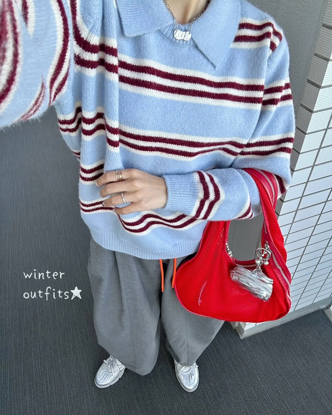 Blue collared striped sweater, voluminous gray trousers, red bag, and silver sneakers