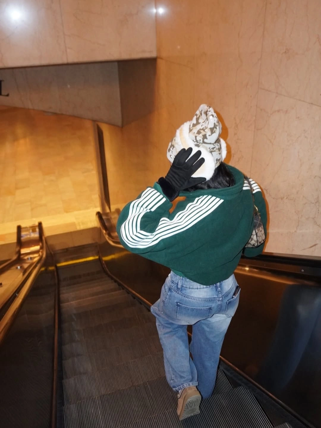 Green striped pullover, faded jeans, patterned white hat, and black gloves