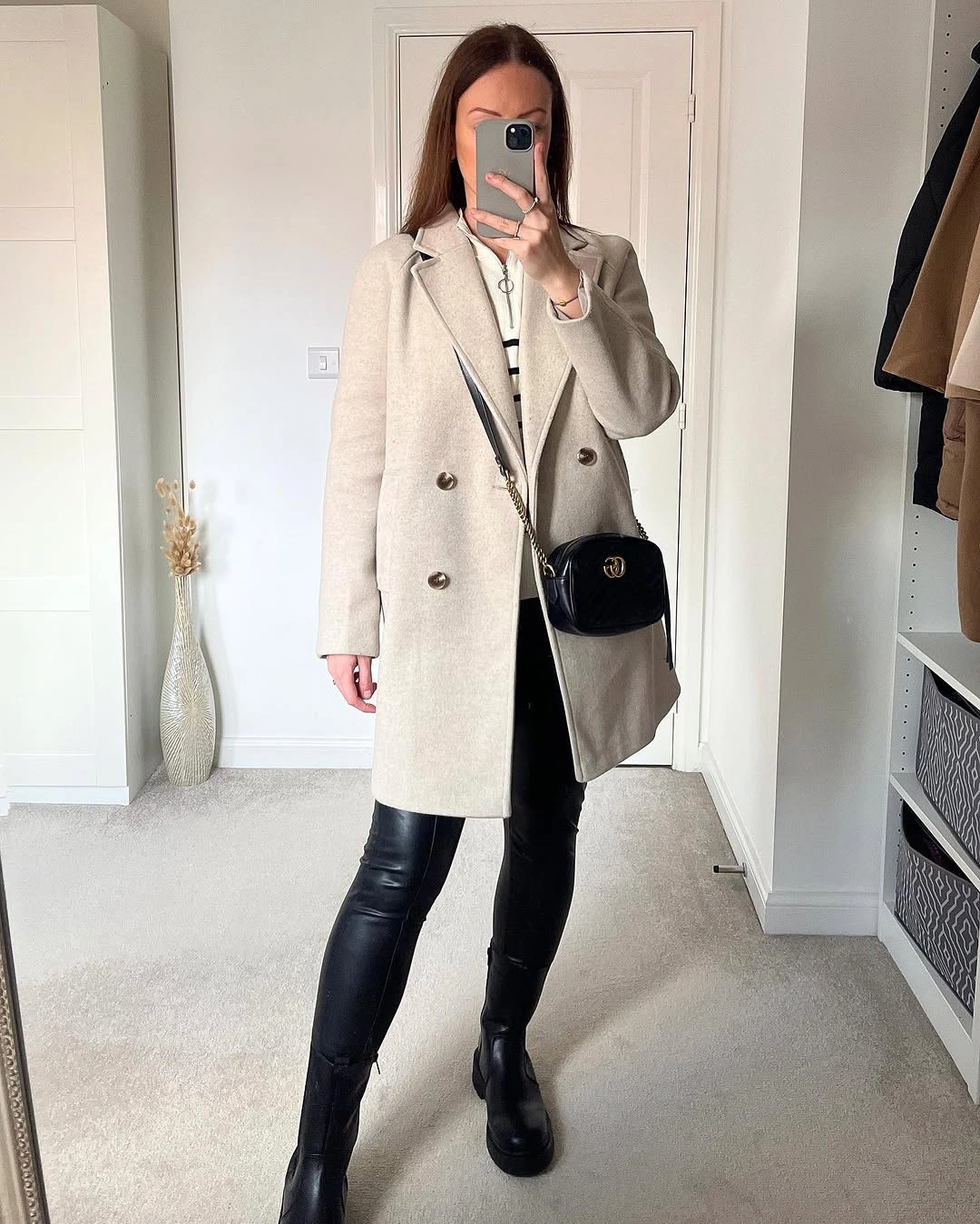 Beige double-breasted coat over black fitted legwear with crossbody bag