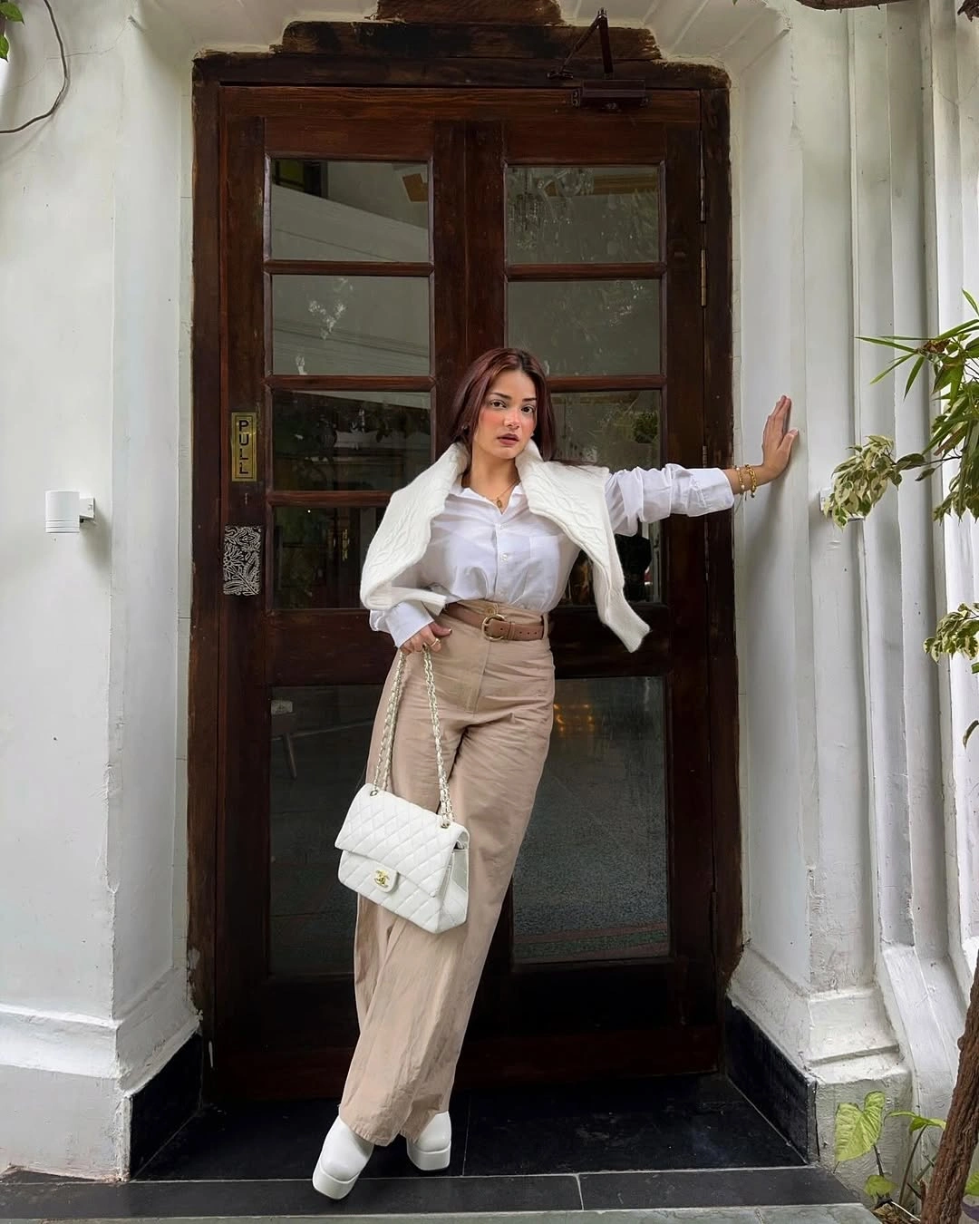 White shirt with shoulder-draped knit beige trousers and quilted handbag