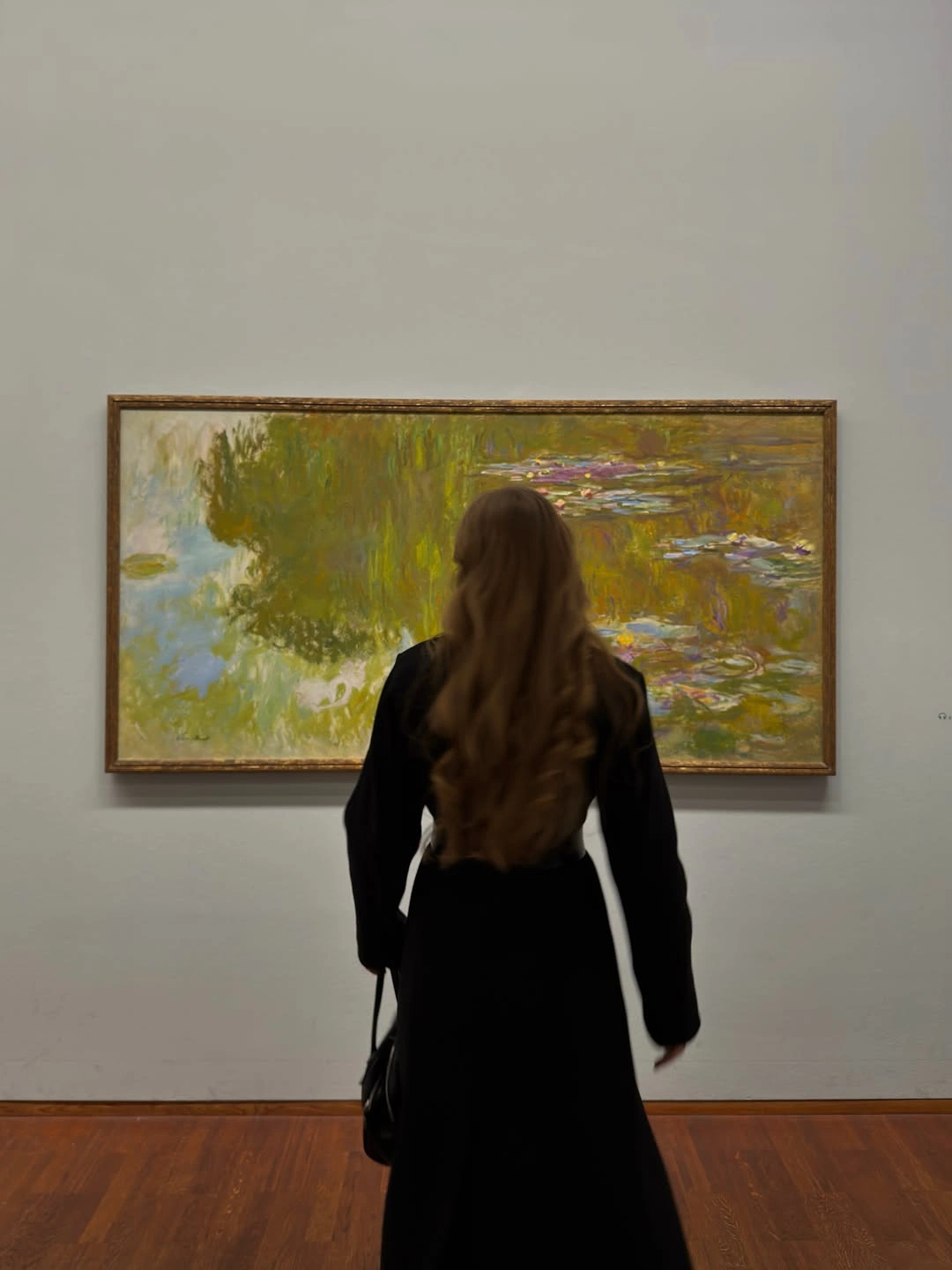 Long black fitted-waist outfit with dark handbag in art gallery