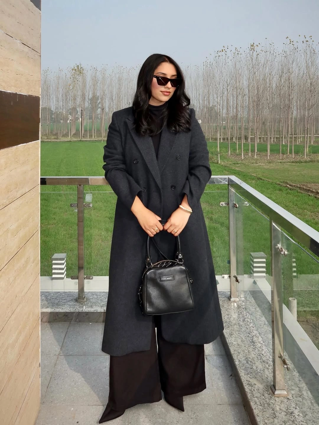 Long charcoal coat over dark clothing with black handbag and sunglasses