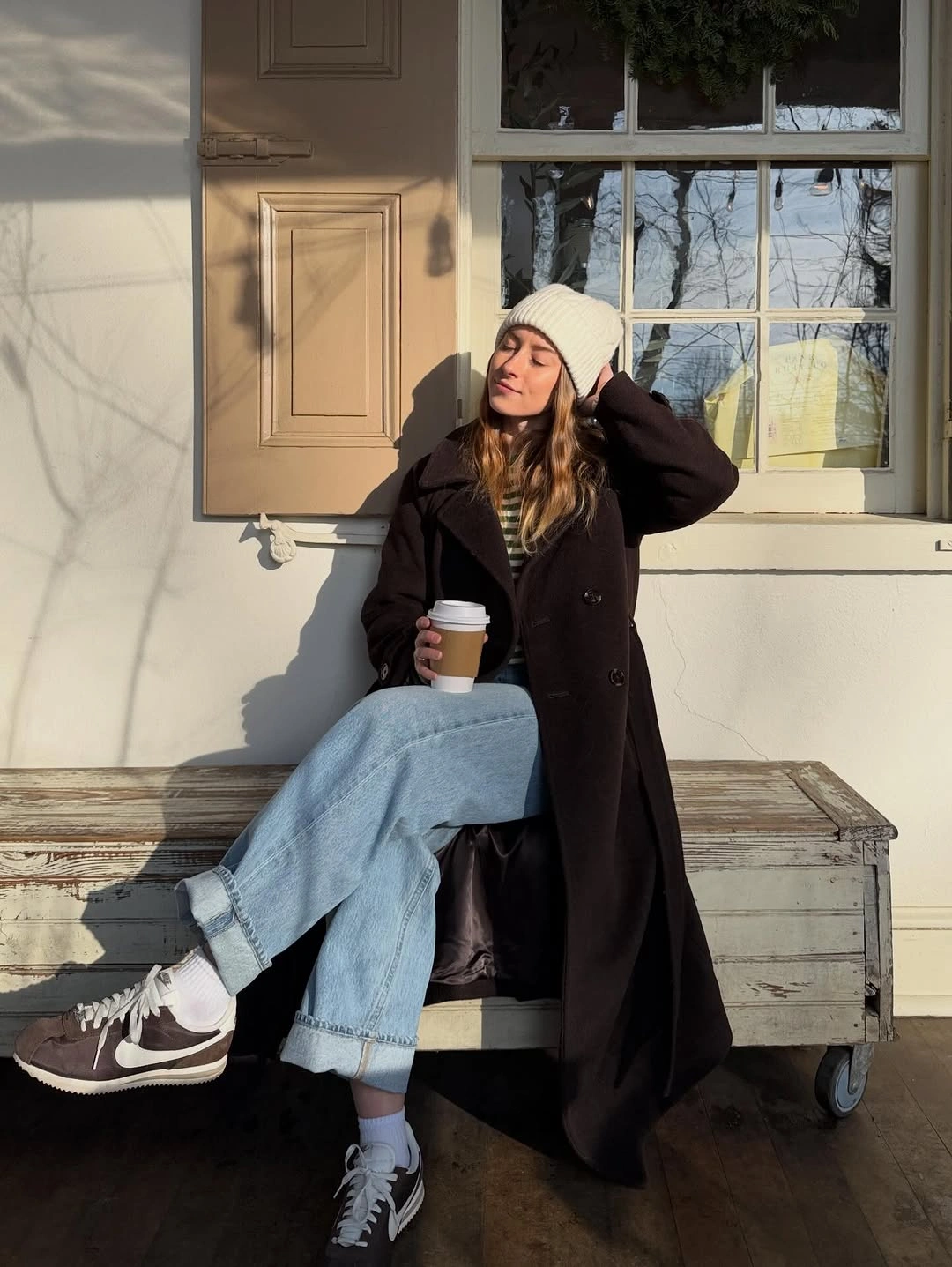 Long dark coat, light blue jeans, pale beanie, and two-tone sneakers