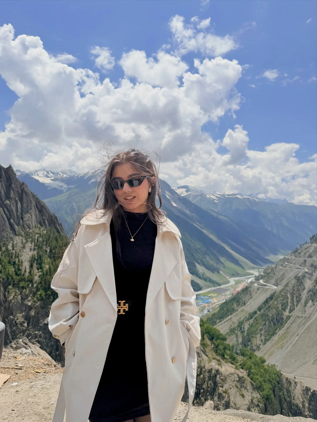 Open cream double-breasted coat over black high-neck clothing with sunglasses