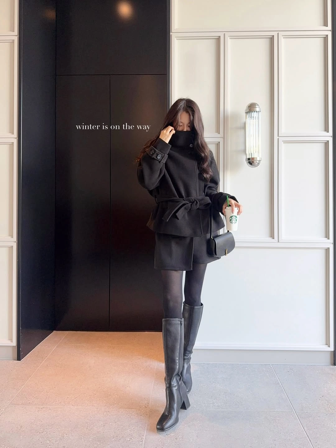 Black loose top and short skirt with dark tights and gray boots