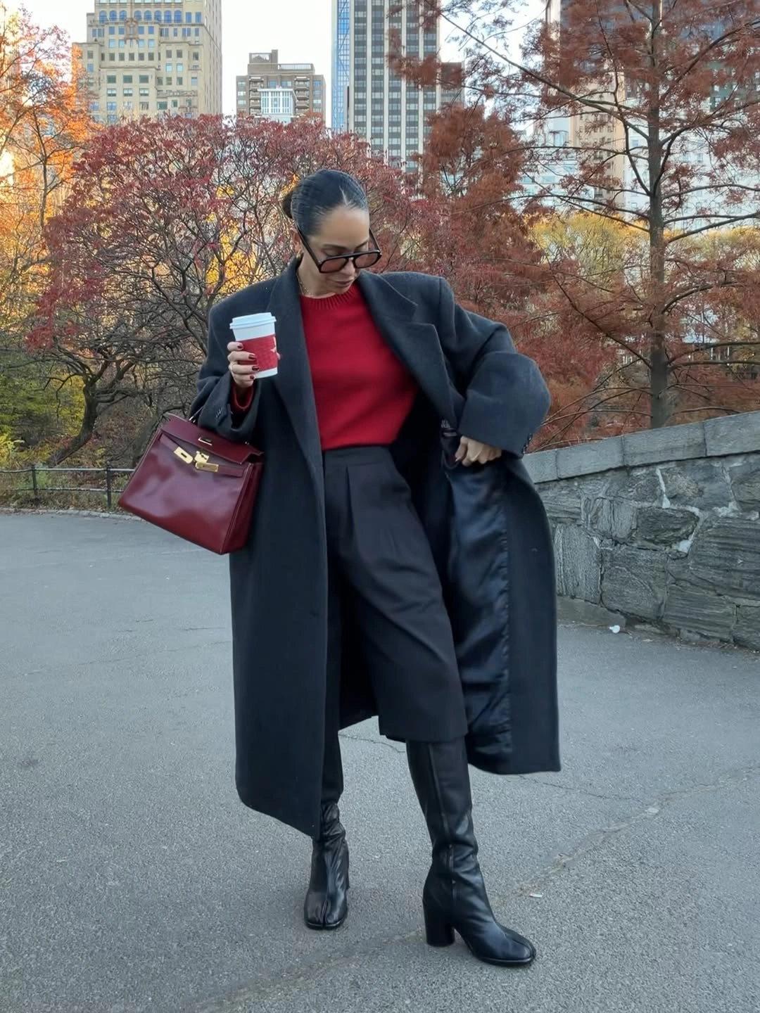 Long charcoal coat over red top with pleated dark bottoms and boots