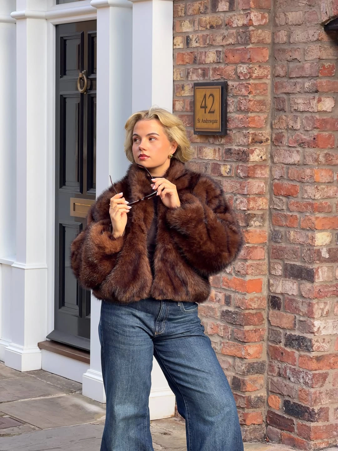 Short brown furry-textured jacket blue wide-leg jeans and sunglasses