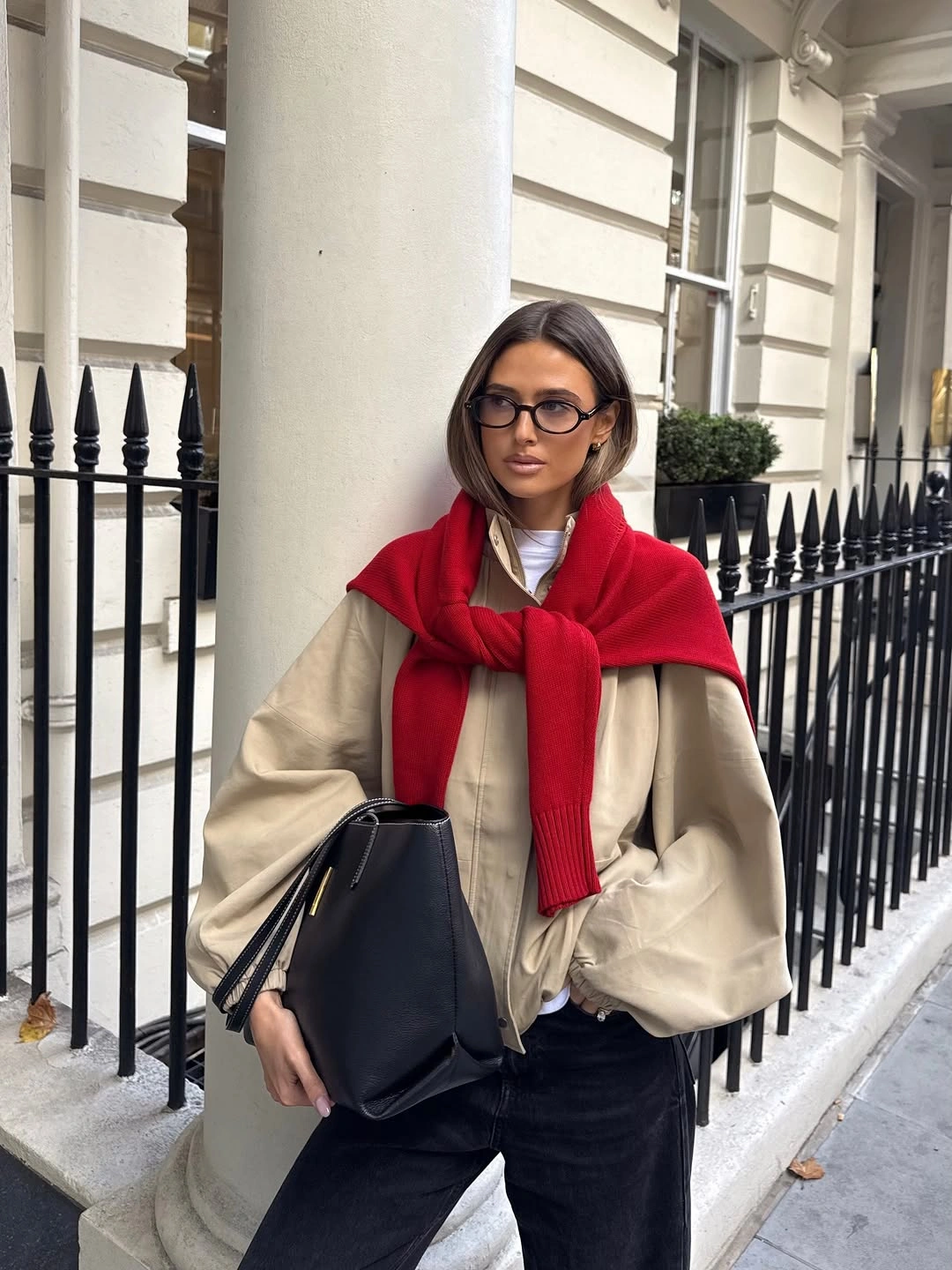 Cream oversized jacket with red shoulder sweater black jeans and handbag