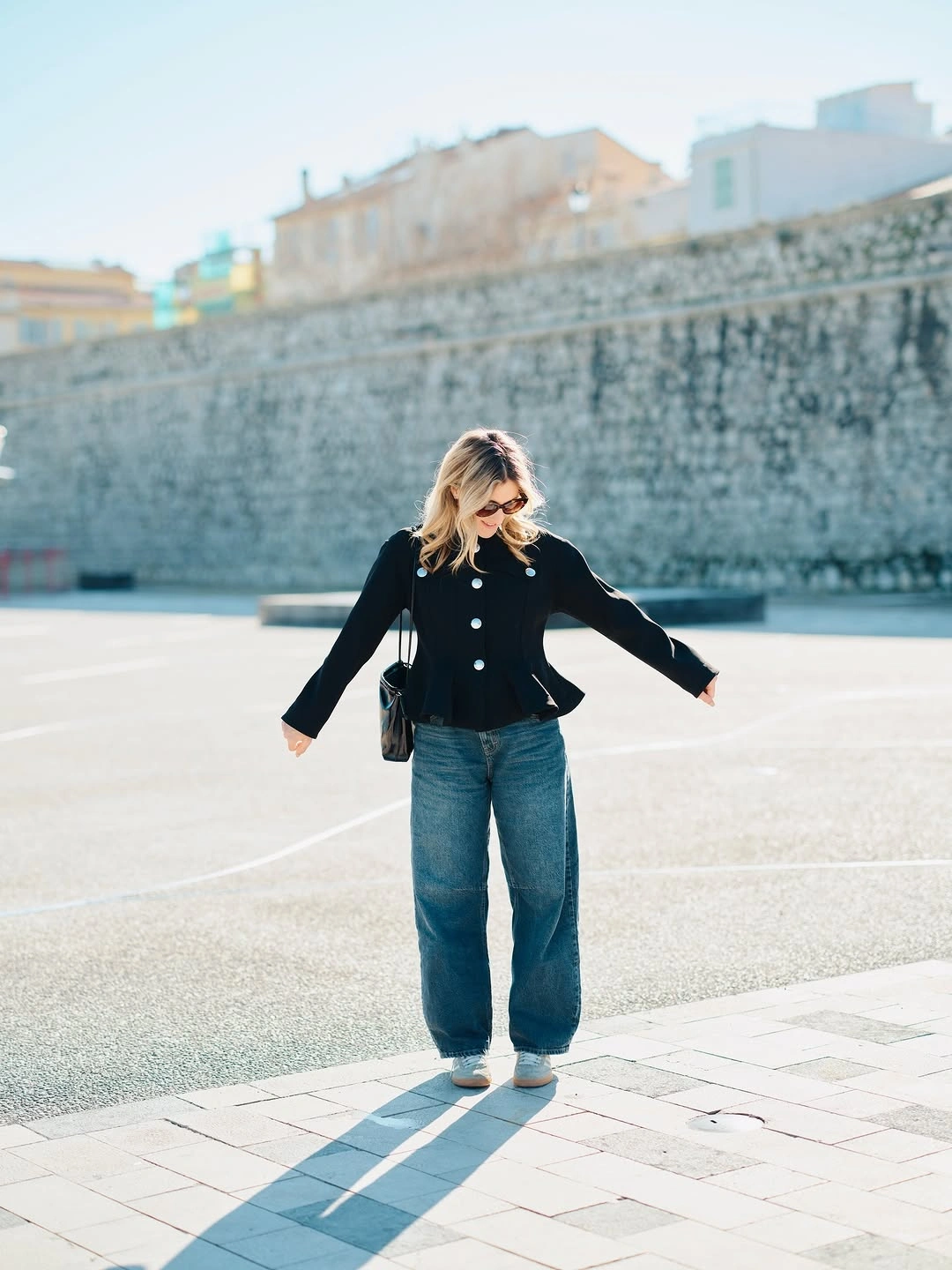 Short black jacket with light buttons loose blue jeans and pale shoes