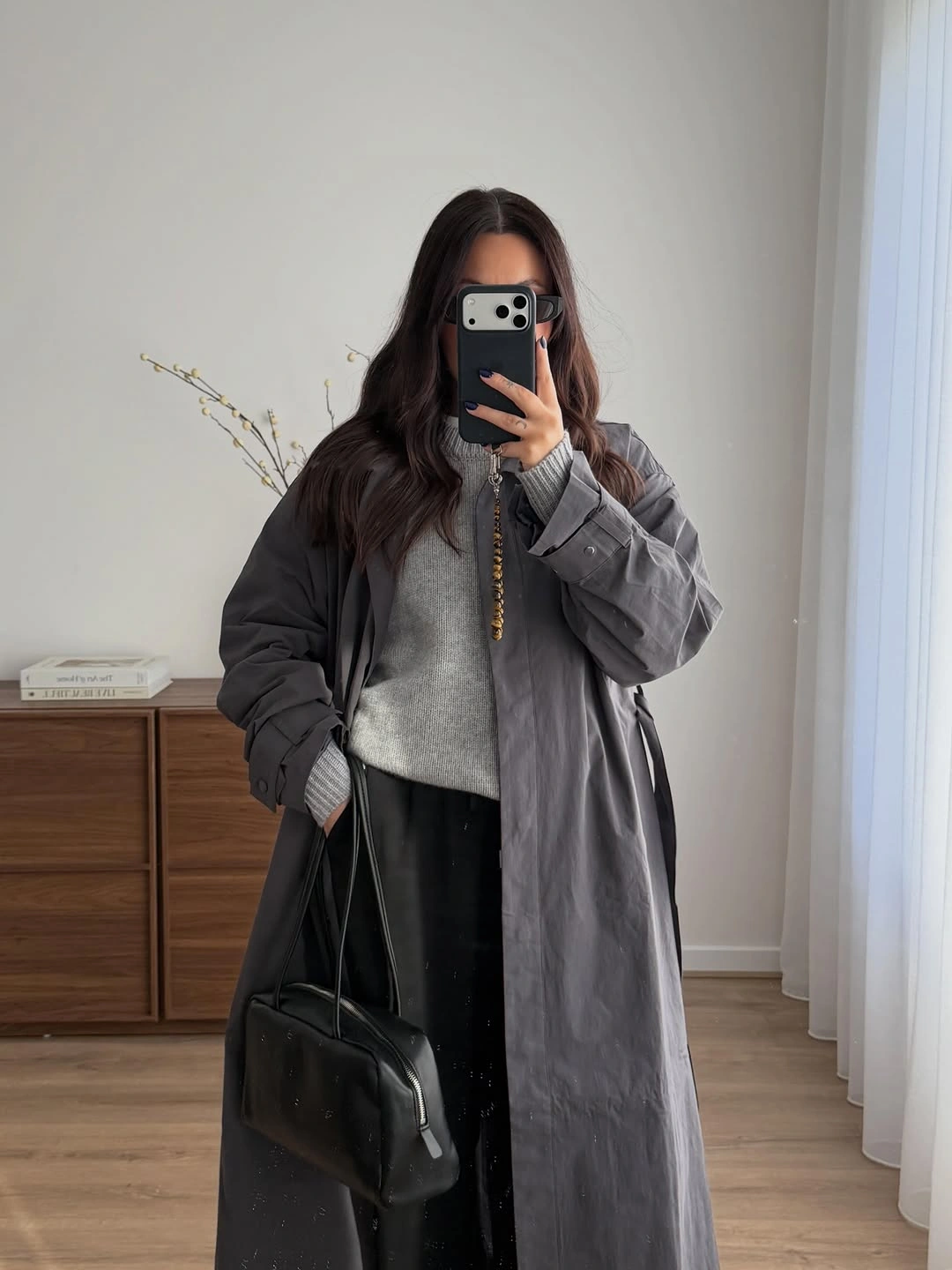 Long gray coat over lighter knit with dark bottoms and black bag