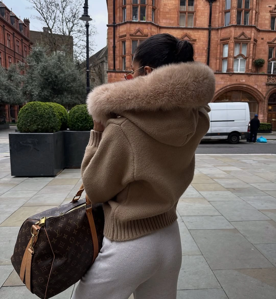 Camel hooded jacket with oversized fluffy trim pale trousers and patterned handbag