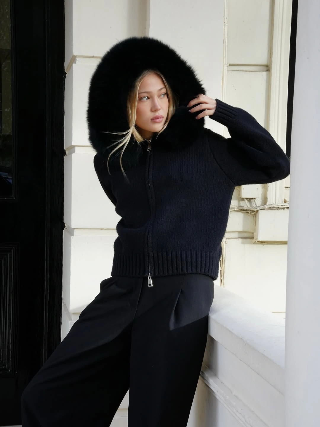 Black zip-front knit with oversized fluffy hood and loose black trousers